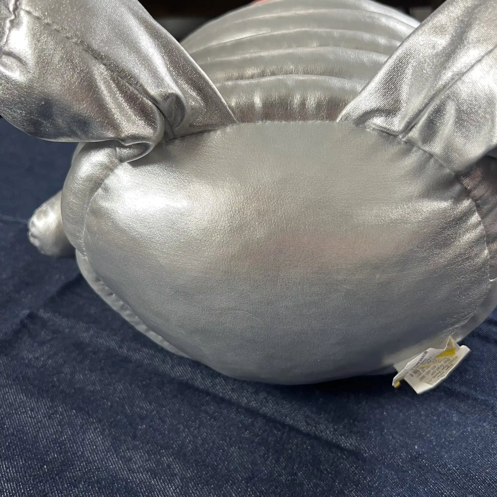 A close-up of a shiny silver plush toy, showing its textured fabric and stitched details, resting on a dark blue denim surface.