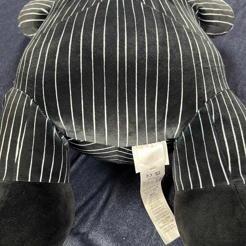 Close-up of a plush toy's stomach and legs, featuring a black and white pinstripe pattern with solid black feet, resting on a blue textured fabric background.