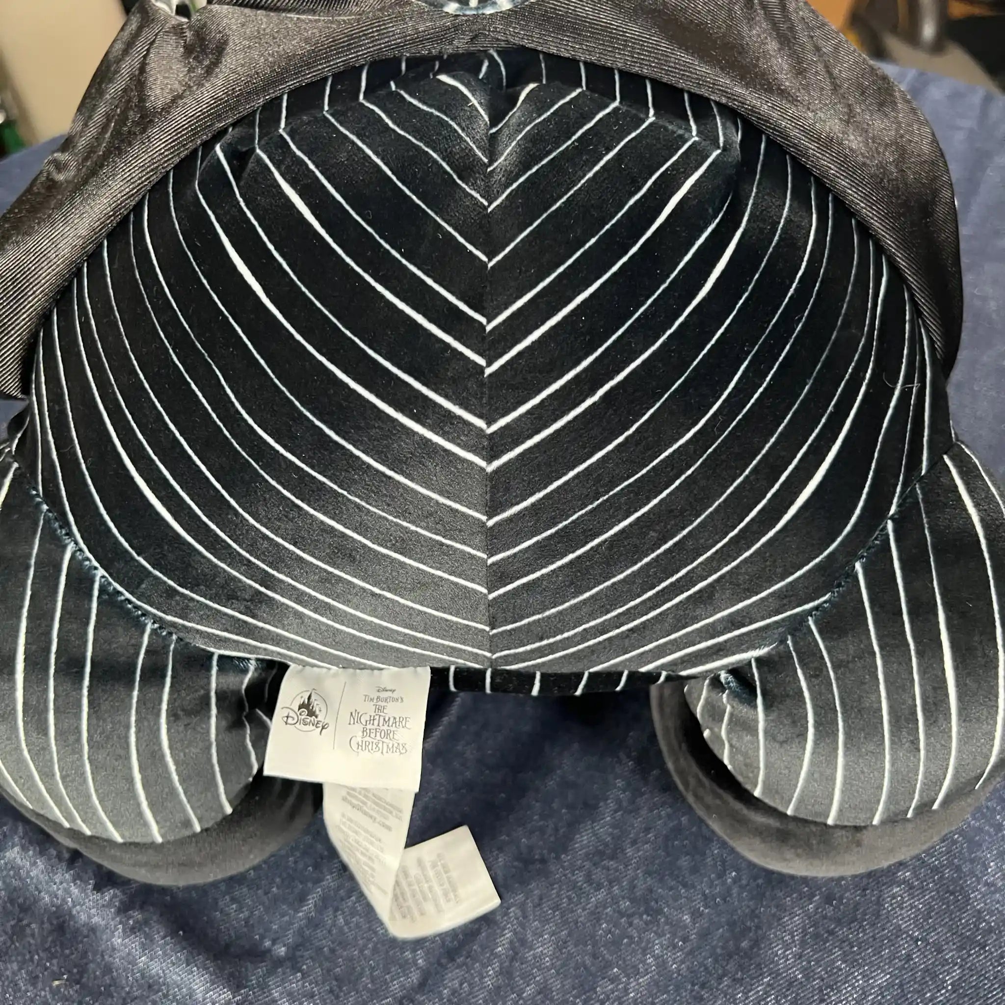 Close-up of a plush toy's backside and legs, featuring a black and white pinstripe pattern with solid black feet, resting on a blue textured fabric background.