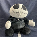 A plush toy of Jack Skellington from The Nightmare Before Christmas, wearing his black and white pinstripe suit, sitting against a blue textured fabric background.