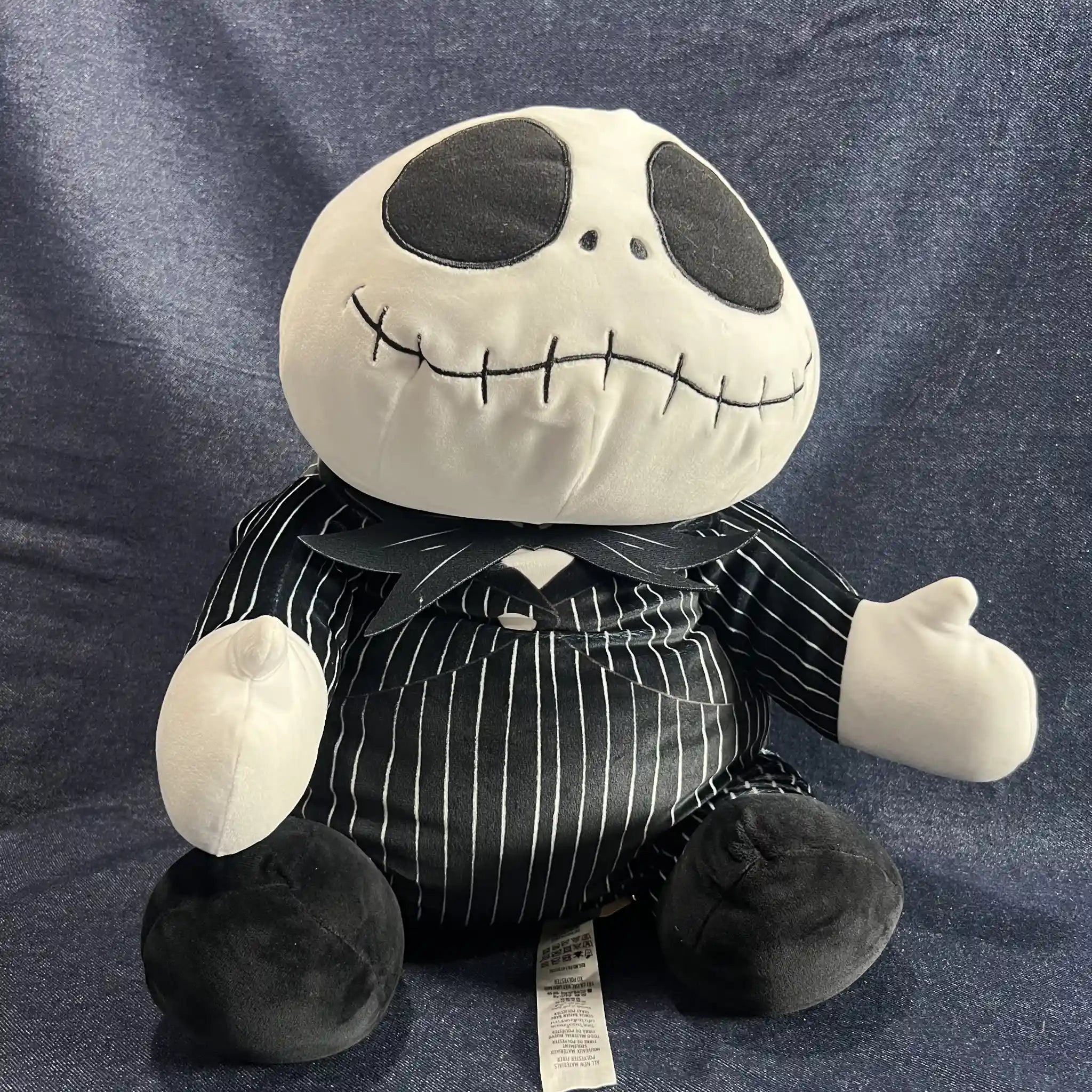 A plush toy of Jack Skellington from The Nightmare Before Christmas, wearing his black and white pinstripe suit, sitting against a blue textured fabric background.